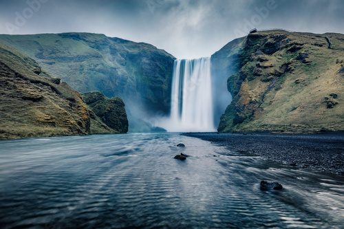 Fototapeta Ciemny nocny widok wodospadu Skogafoss. Fantastyczny letni krajobraz rzeki Skoga. Niesamowita scena plenerowa Islandii, Europy. Piękno natury w tle.