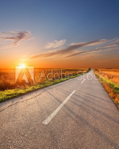Fototapeta Jadący na pustej aspalt drodze przy zmierzchem