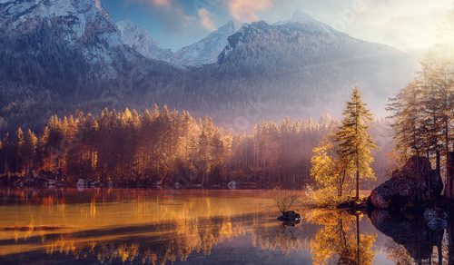 Fototapeta Niesamowita sceneria natury. Piękny krajobraz z wysokimi górami z oświetlonymi szczytami, kamieniami w górskim jeziorze, odbiciem, błękitnym niebem i żółtym światłem słonecznym o wschodzie słońca. Niesamowite tło natury.