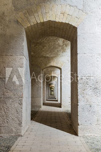 Fototapeta Wnętrze tunelu zamkowego z szeregiem symetrycznych łuków w twierdzy bastionowej.