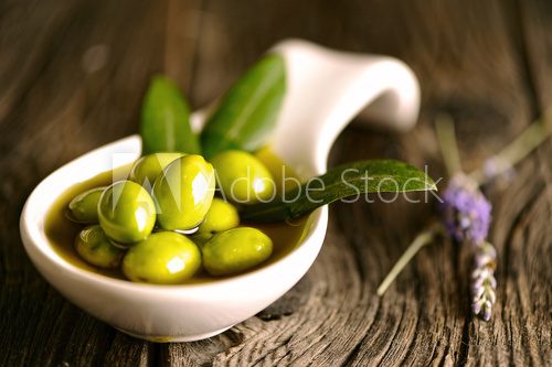 Obraz Zielone oliwki w pucharze i gałązka oliwna na drewnianym stole