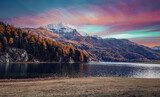 Fototapeta Cudowny jesienny krajobraz podczas zachodu słońca. Bajkowe górskie jezioro z malowniczym niebem, majestatycznym skalistym wierzchowcem i kolorowymi drzewami w słońcu. Niesamowita sceneria przyrody. Jezioro Champfer. Szwajcaria Alpy