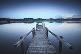 Fototapeta Drewniany molo lub jetty na błękitnym jeziornym zmierzchu i nieba odbiciu dalej